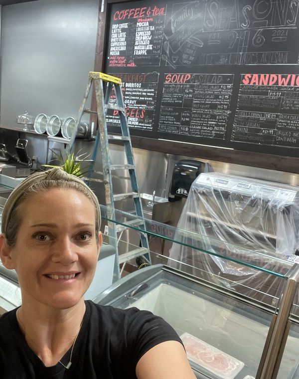 Kelli in front of a large hand-lettered cafe chalkboard menu she painted