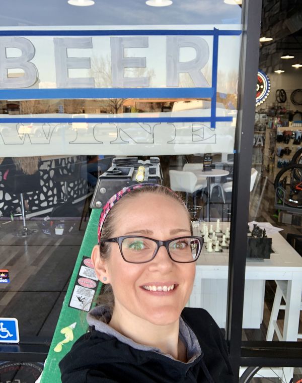 Kelli outside a storefront window she is lettering with the words beer and wine